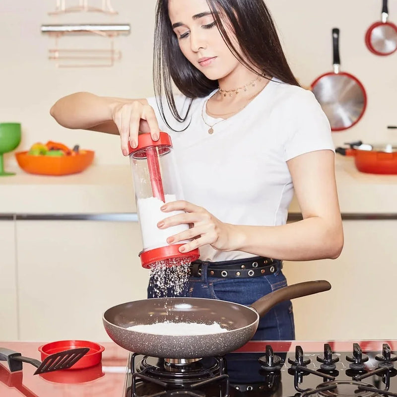 mulher com tapioqueira com peneira e copo transparente polvilhando goma de tapioca uniforme direto na frigideira